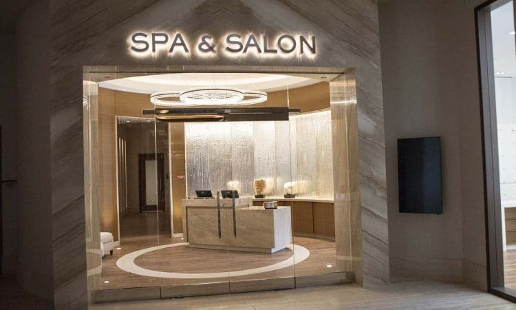 Entrance to a modern spa and salon with illuminated sign, marble walls, glass doors, and a reception desk inside.