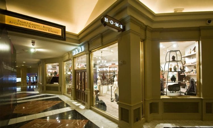 A retail store labeled "HOME" displays various home decor items inside a well-lit shopping mall corridor with marble flooring and overhead signage.