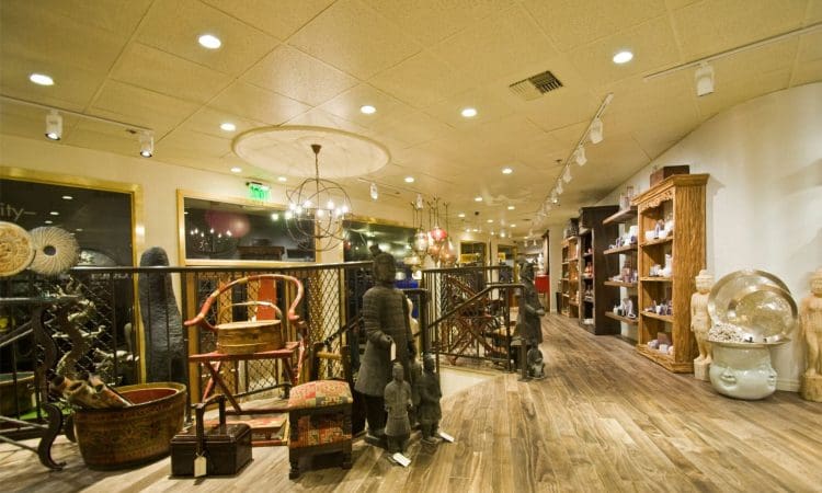 A well-lit store interior features wooden flooring, shelves with decorative items, sculptures, and furniture arranged neatly throughout the space.