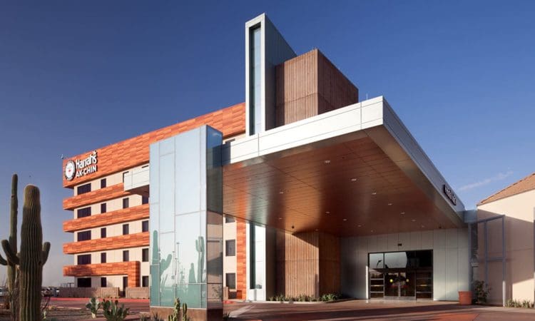 Modern multi-story building with a large covered entrance, desert landscaping, and signage that reads "Harrah’s Ak-Chin" on the exterior.