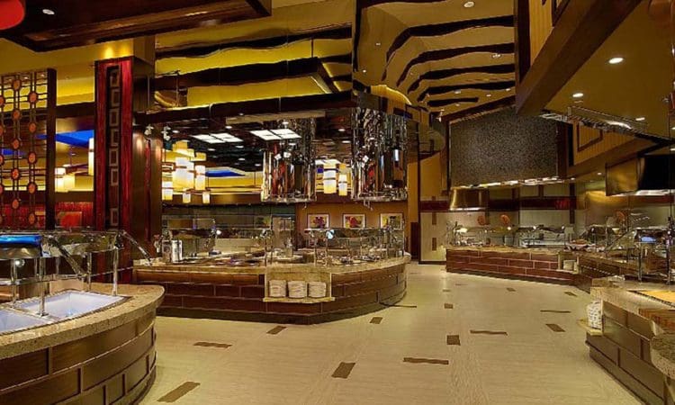 Modern buffet restaurant interior with empty food stations, curved serving counters, warm lighting, and decorative ceiling elements.