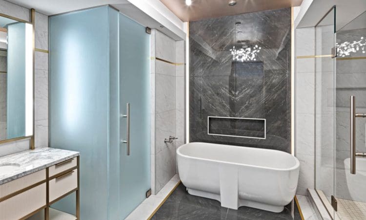 Modern bathroom with a white freestanding tub, black marble accent wall, glass shower, marble floors, vanity with sink, and contemporary lighting fixture.