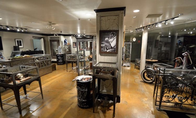 A motorcycle-themed showroom with display cases, framed photos on the walls, and a motorcycle partially visible on the right side. The floor is polished and the lighting is bright.