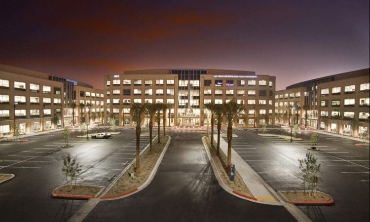 Large modern office building with three wings, palm trees lining the entrance, and an empty parking lot at dusk.