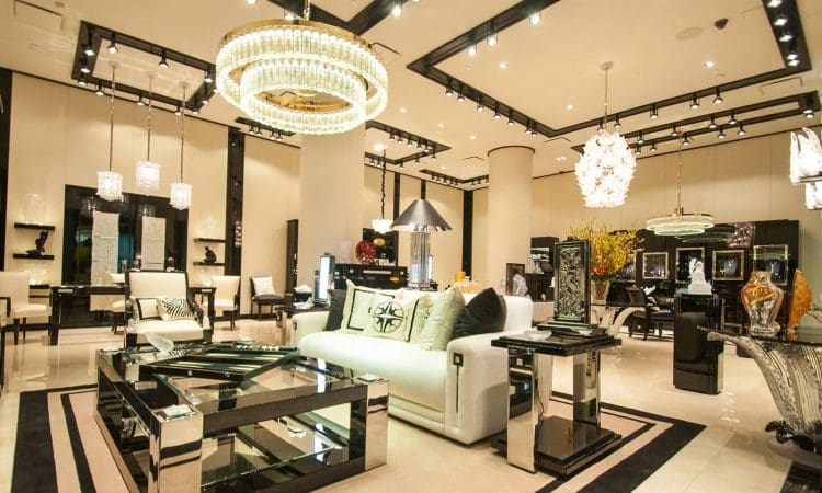 A modern luxury furniture showroom with chandeliers, glass tables, sofas, and decorative items displayed under bright lighting.