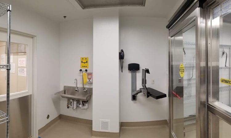 A clean laboratory room with a metal sink, soap and towel dispensers, and stainless steel shelves behind glass doors labeled "automatic.