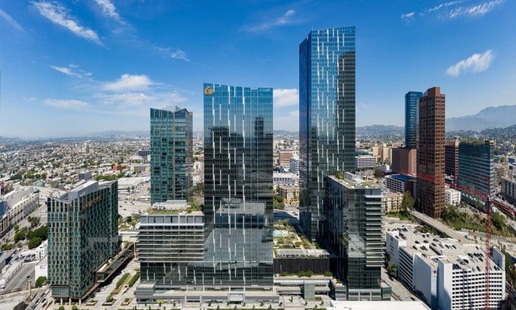 Aerial view of modern high-rise office buildings in a downtown urban area with clear skies and mountains in the background.