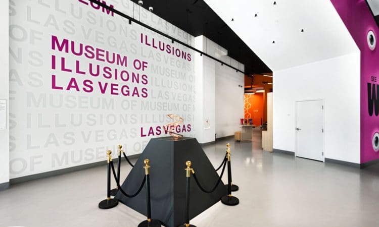 Interior of the Museum of Illusions in Las Vegas featuring a black display pedestal with a basketball enclosed by stanchions, and museum signage on white walls.