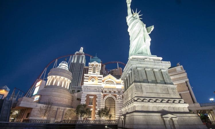 A replica of the Statue of Liberty stands in front of New York-themed buildings and a roller coaster at the New York-New York Hotel in Las Vegas at night.