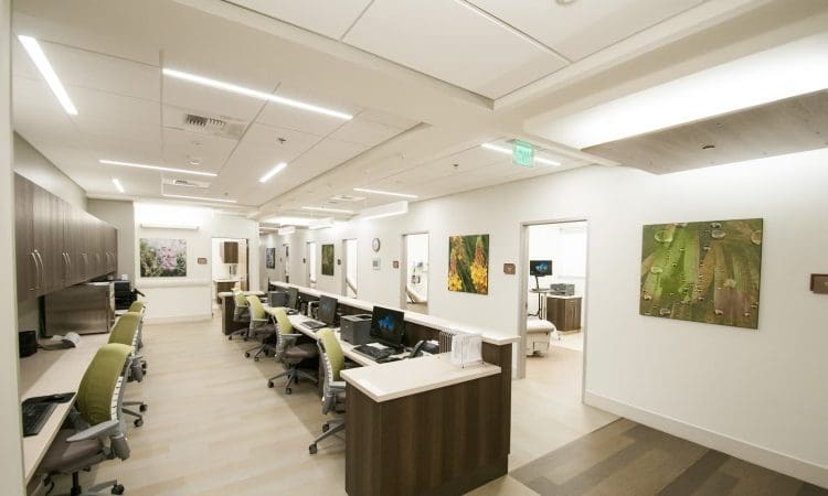 A modern medical office with multiple workstations, computers, green chairs, wall art, and bright overhead lighting.