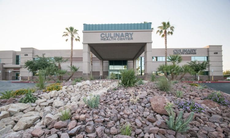 Front view of the Culinary Health Center building with landscaped rocks, desert plants, and palm trees in the foreground.