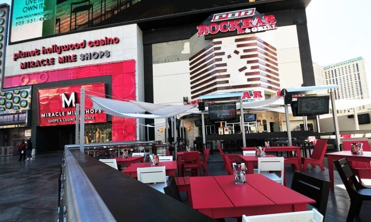 Outdoor dining area with red and white tables and chairs in front of PBR Rock Bar & Grill, located near Miracle Mile Shops and Planet Hollywood Casino.