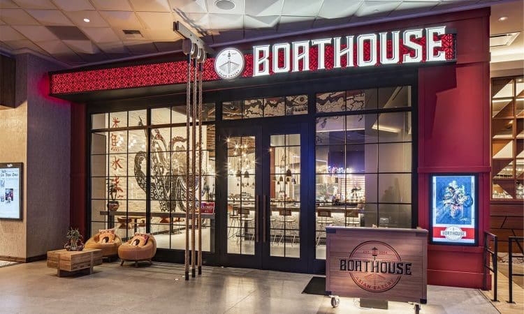 Exterior view of Boathouse restaurant with large glass doors, illuminated sign, nautical-themed decor, and a reception desk near the entrance.