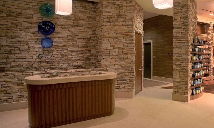 Reception desk with a stone wall background, decorative glass plates, and shelves with products in a modern, softly lit interior.