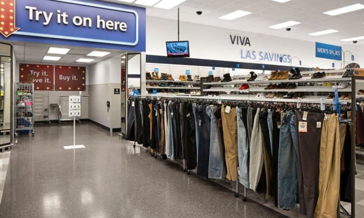 Clothing racks with pants and jeans in a retail store; a large "Try it on here" sign points to fitting rooms in the background.