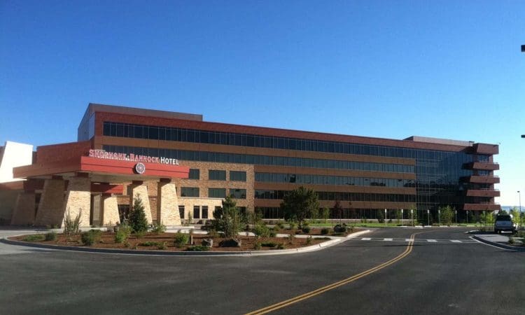 A modern, multi-story hotel building with "Snoqualmie Ramada Hotel" signage, featuring large windows and a red-brown exterior, set against a clear blue sky.
