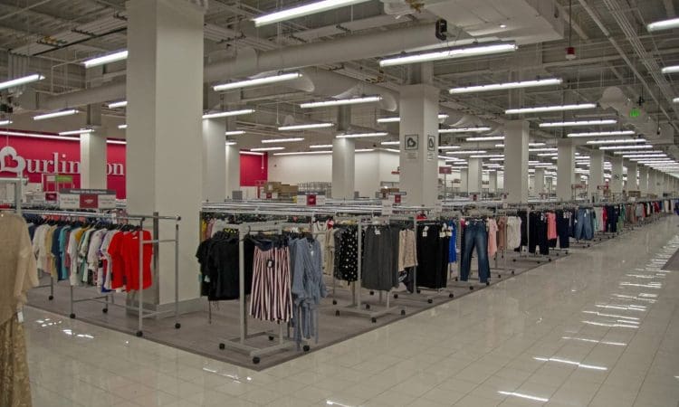 Interior of a brightly lit retail clothing store with racks of assorted clothes and tiled floors.