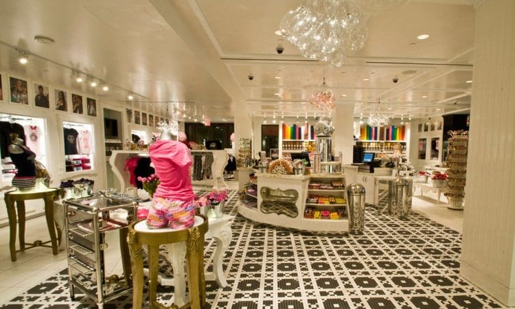Brightly lit boutique store interior with patterned tile floor, displays of clothing, accessories, and candy, and mannequins wearing colorful outfits.