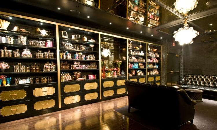 Luxurious candy shop interior with dark wood floors, gold-accented shelves filled with jars of sweets, and elegant seating under a chandelier.