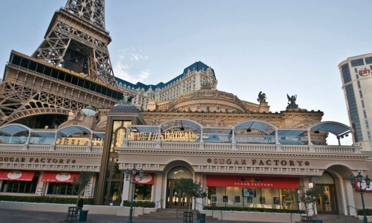 The exterior of the Sugar Factory restaurant at the Paris Las Vegas Hotel, with the Eiffel Tower replica and ornate architecture visible in the background.