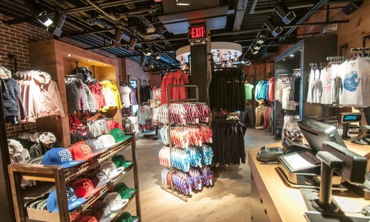 Clothing store interior with racks of shirts, jackets, and hats neatly displayed, and a checkout counter in the foreground.
