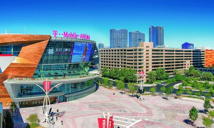 T-Mobile Arena is shown next to a multi-story parking garage and landscaped plaza constructed by PENTA on a clear, sunny day with tall buildings in the background.