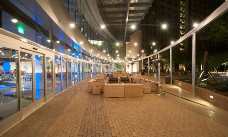Outdoor patio area at night with wicker seating arrangements, string lights overhead, and glass doors leading to an indoor space with blue lighting.