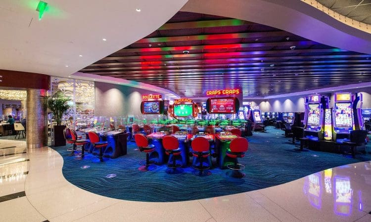 Casino interior with empty red chairs around gaming tables, slot machines, and colorful lights illuminating the space.