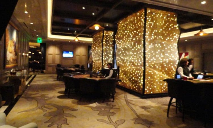 A dimly lit casino interior with two large, illuminated panels, several gaming tables, and staff in uniforms.