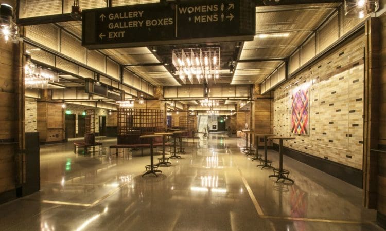 Spacious, modern lobby with polished floors, wooden accents, wall art, chandeliers, and overhead signs directing to galleries, restrooms, and exit.