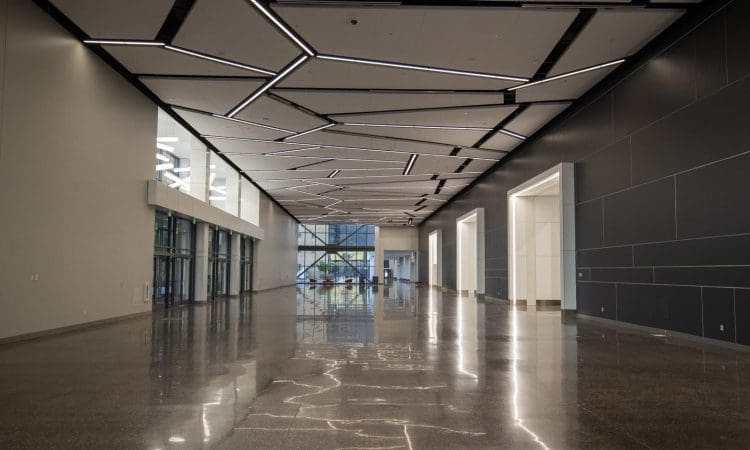 Spacious, modern lobby with geometric ceiling lights, polished floor, large windows, and dark accent walls.