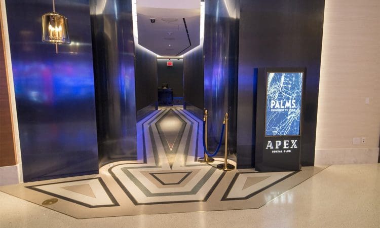 Entrance to Apex Social Club at Palms, featuring geometric floor patterns, dark walls, a digital sign, and a small rope barrier.