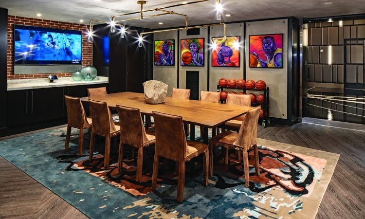 Modern dining room with a wooden table, leather chairs, basketballs stacked against the wall, sports-themed artwork, a TV, and contemporary lighting.