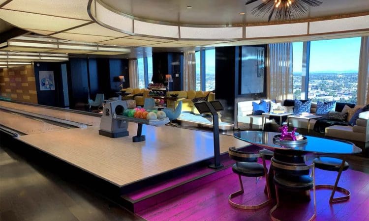 A modern living space with a built-in bowling alley, colorful seating area, large windows with city views, and a round table with four chairs on a magenta rug.