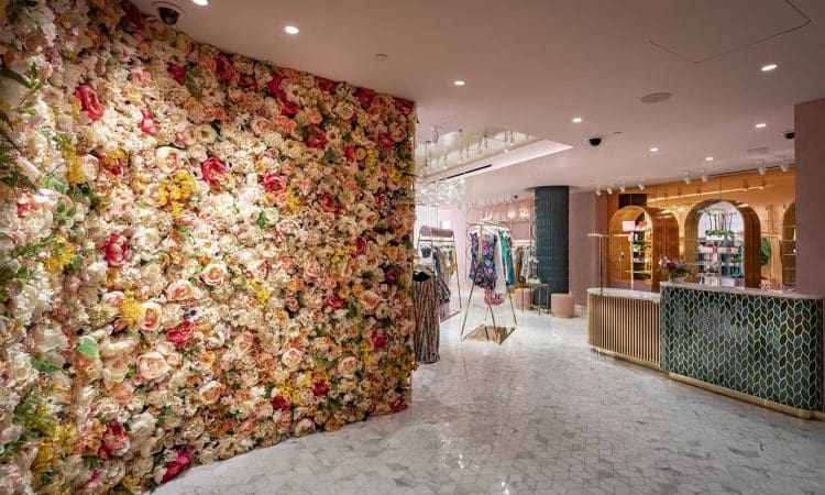 Interior of a boutique with a wall covered in artificial flowers, marble flooring, clothing racks, and a modern, stylish decor.