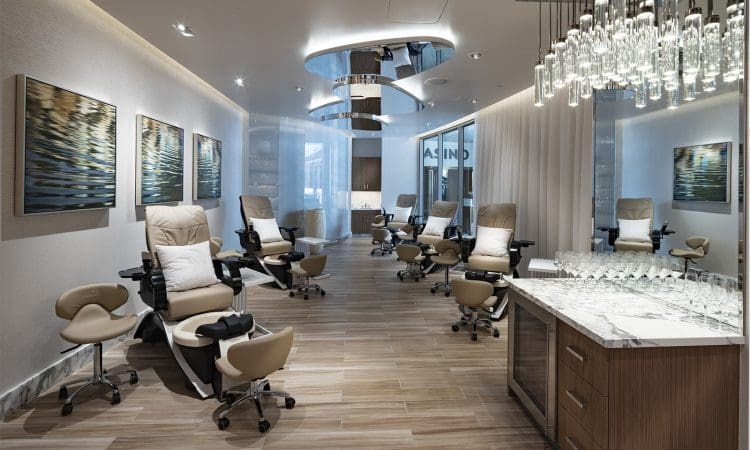 Modern spa room with reclining chairs, stools, a marble counter with glassware, and wall art; wood flooring and mirrored ceiling panels enhance the space.
