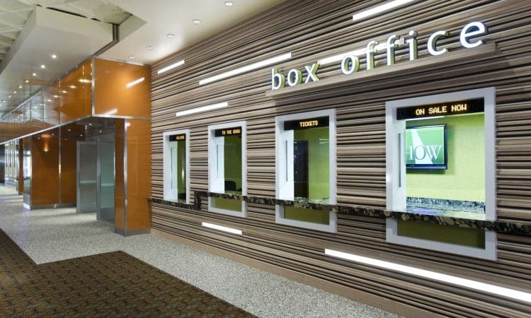 Modern box office with multiple ticket windows, sleek wall paneling, digital screens displaying show information, and overhead sign reading "box office.