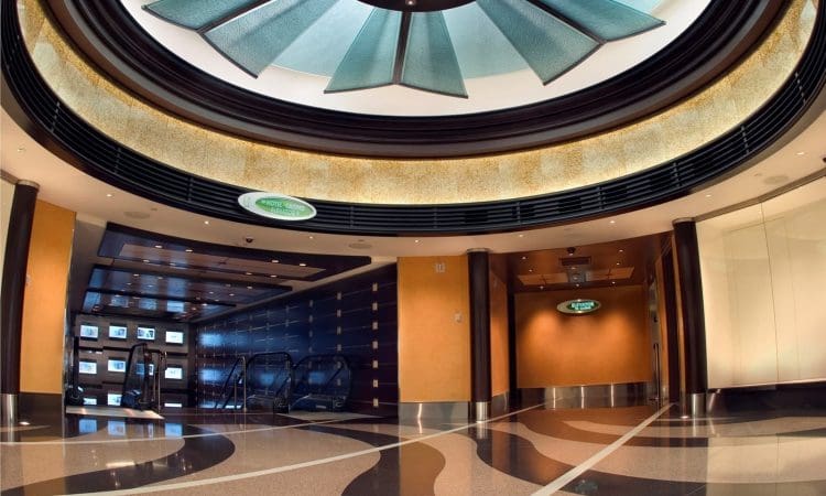 Modern indoor lobby with patterned flooring, escalators on the left, and a large decorative ceiling feature with glass panels.