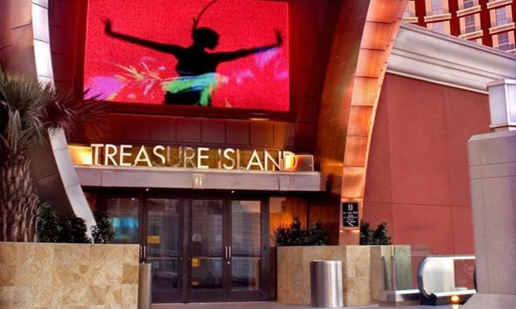Entrance to Treasure Island with glass doors, a large red digital screen displaying a dancer silhouette above, and plants flanking the entryway.