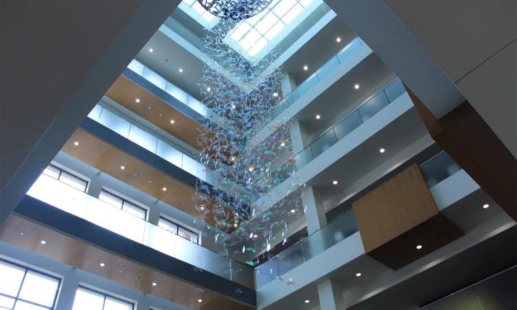 An atrium with multiple floors, large windows, and a hanging glass or acrylic sculpture suspended from the ceiling.