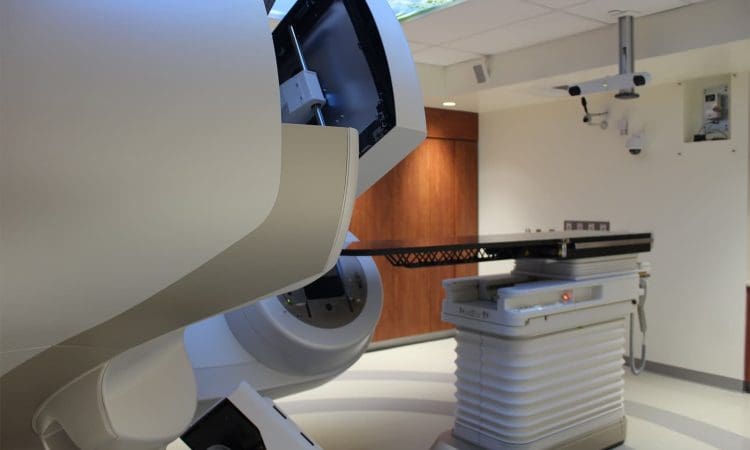 A medical treatment room with a robotic linear accelerator and patient table used for radiation therapy.