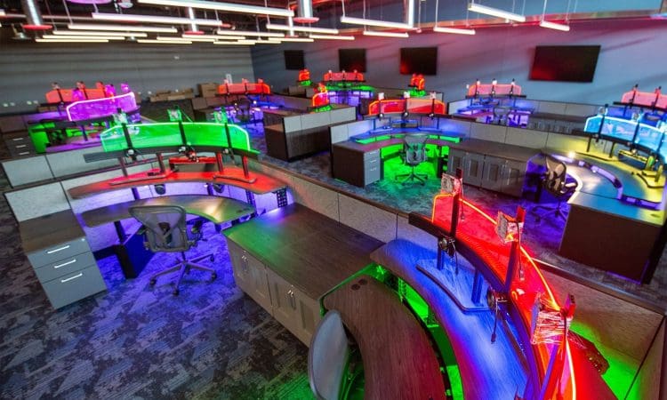 Via Inspirada Police Station office space with curved desks, ergonomic chairs, and colorful LED lighting under each workstation in an open-plan layout. Multiple monitors and overhead lights are visible.