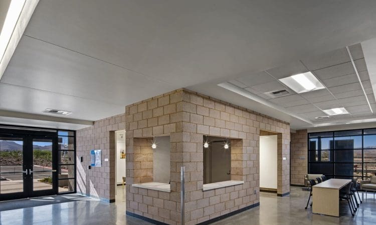 Modern office space with large windows, polished concrete floors, and a central structure made of light-colored concrete blocks; natural light fills the room.