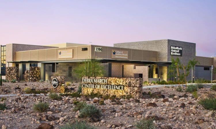 Modern medical facility, "Debra March Center of Excellence," with stone signage, desert landscaping, and clear building labels under a pastel sky.