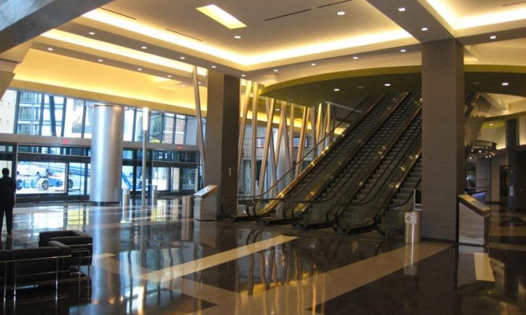 Spacious modern lobby with polished floors, escalators, seating area, large windows, and bright overhead lighting.
