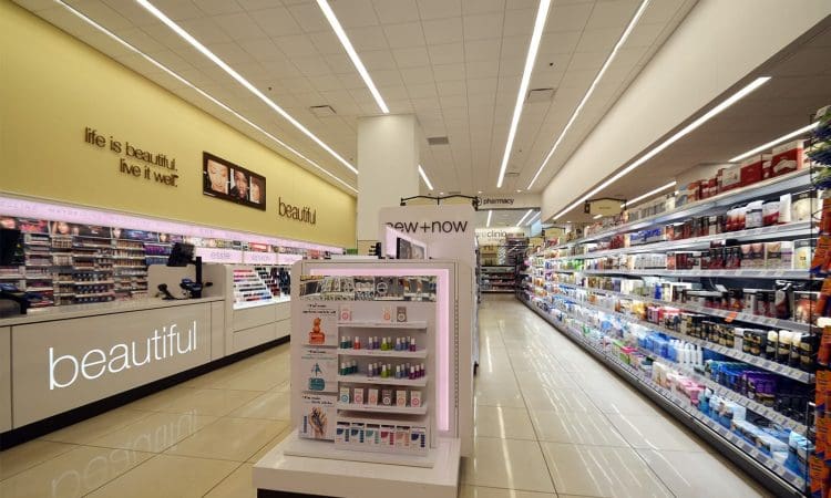 A brightly lit drugstore beauty aisle with skincare and cosmetic displays, shelves of products, and signage reading "beautiful" and "life is beautiful. live it well.