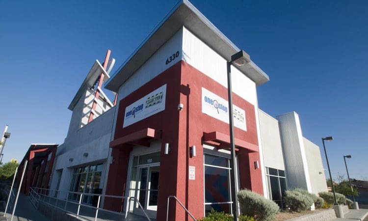 Modern commercial building with red and white exterior, large windows, ramp access, and signage, photographed under a clear blue sky.
