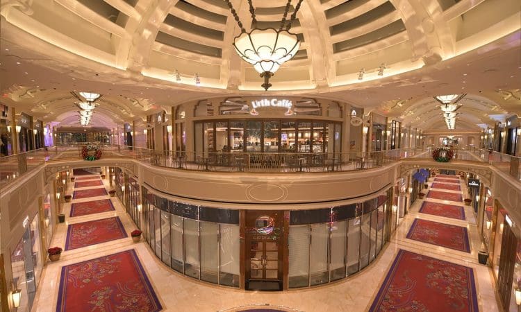 A spacious, well-lit indoor shopping mall with red carpeted walkways, glass railings, and a prominent Urth Caffé located on the upper level.