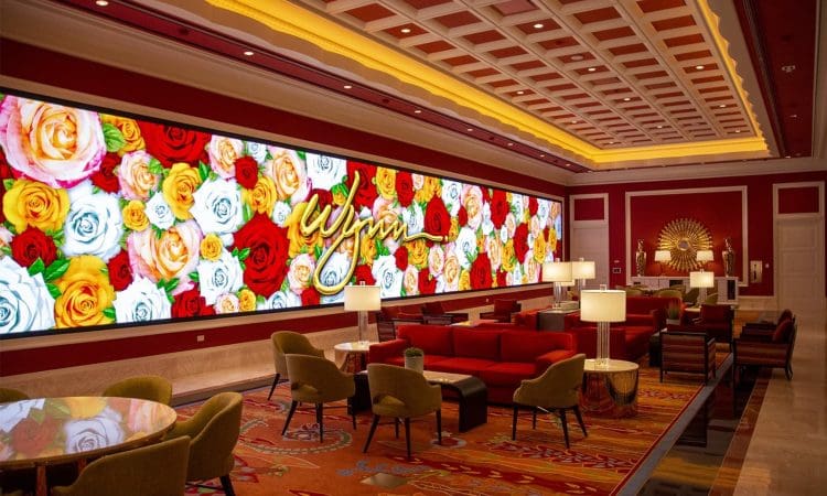 A hotel lounge with red chairs and sofas, floral-patterned carpet, large wall art of colorful roses, and the word "Wynn" displayed in script.
